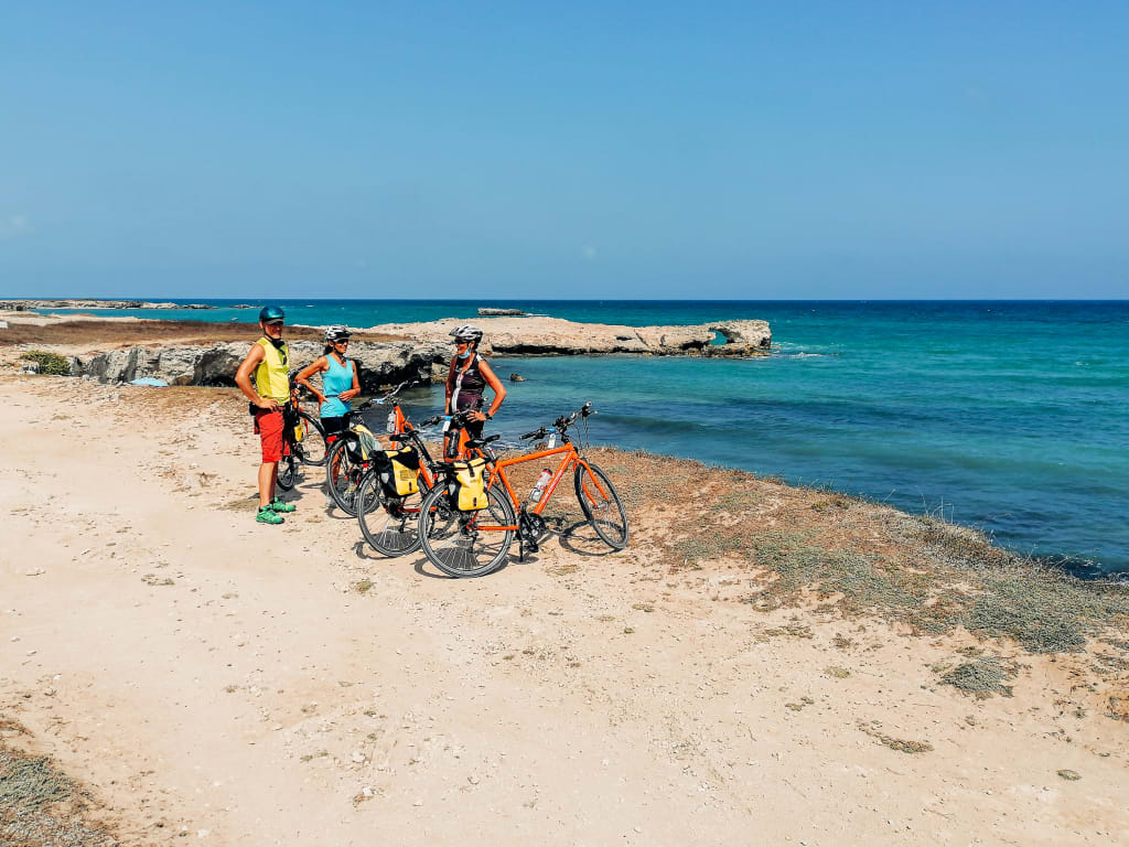 Gruppo di ciclisti in viaggio con "Girolibero" in pausa lungo la costa del Salento, vista sul mare, natura selvaggia